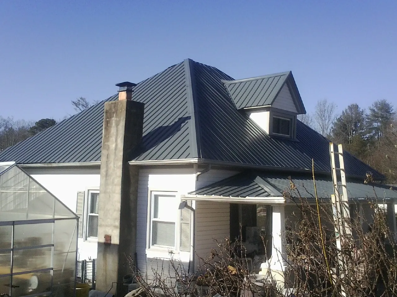 Dark blue standing seam metal roof on a white farmhouse with dormer — Slate & Tile Roof Repair by Roofing Brothers in Westland