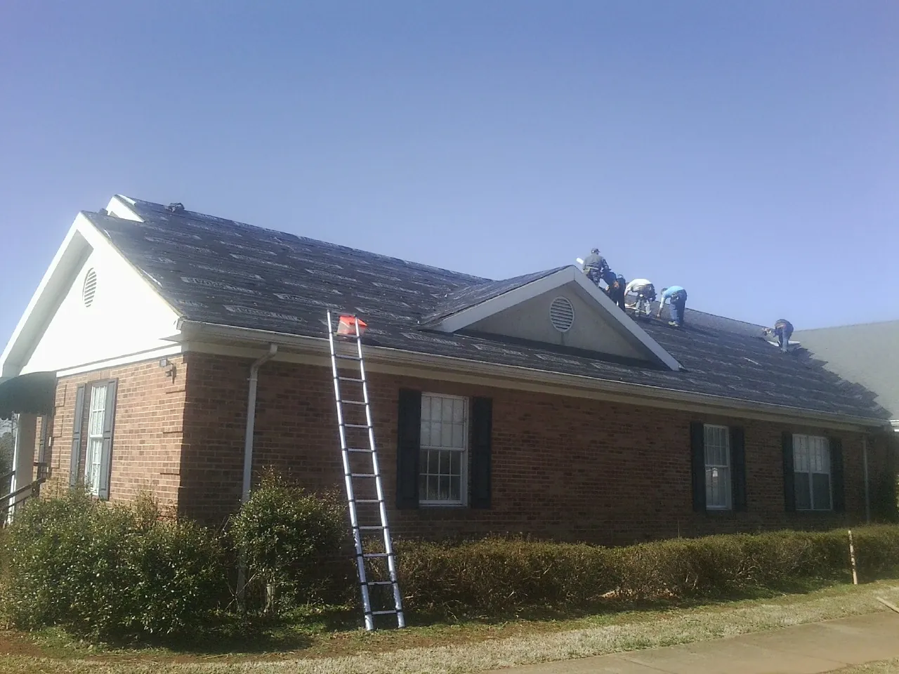 Crew tearing shingles off a brick ranch roof with a ladder set — Metal Roof Repair work by our crew in Westland