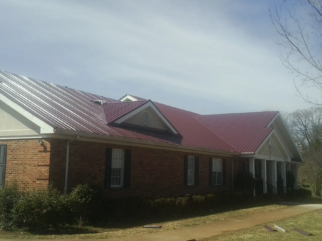 Red metal roof with gabled entries on a long brick building, from a Hail Damage Roof Repair job in Westland