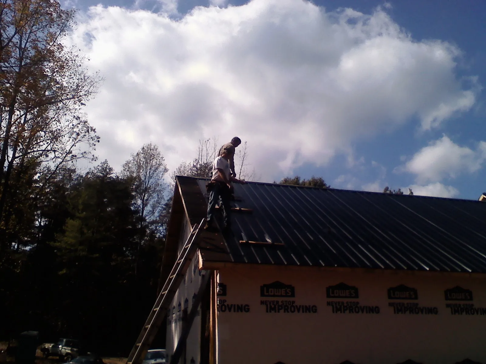 Roofer fastening dark metal panels high against a cloudy sky, from a Roof Inspection job in Westland