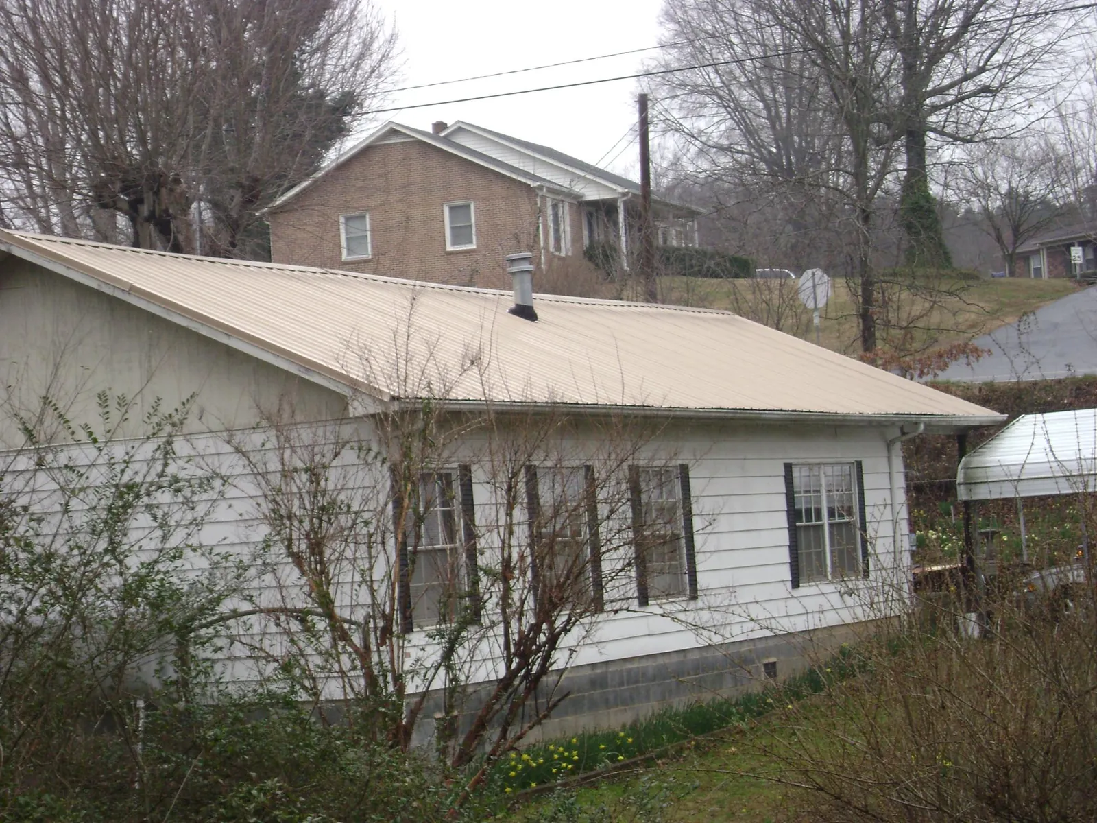 Tan metal roof on a white sided house set into a hillside — Commercial Roofing by Roofing Brothers in Westland